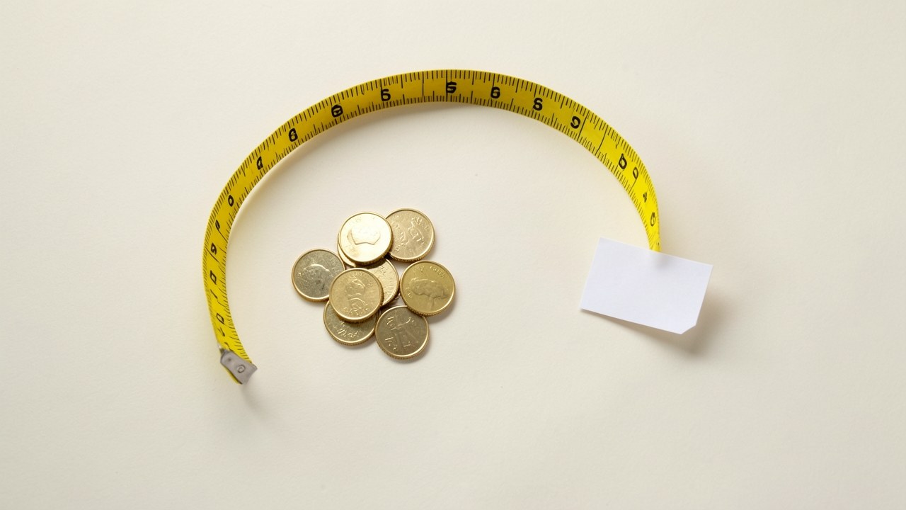 A small pile of gold coins next to a measuring tape and a blank label, symbolizing loan amount determination.